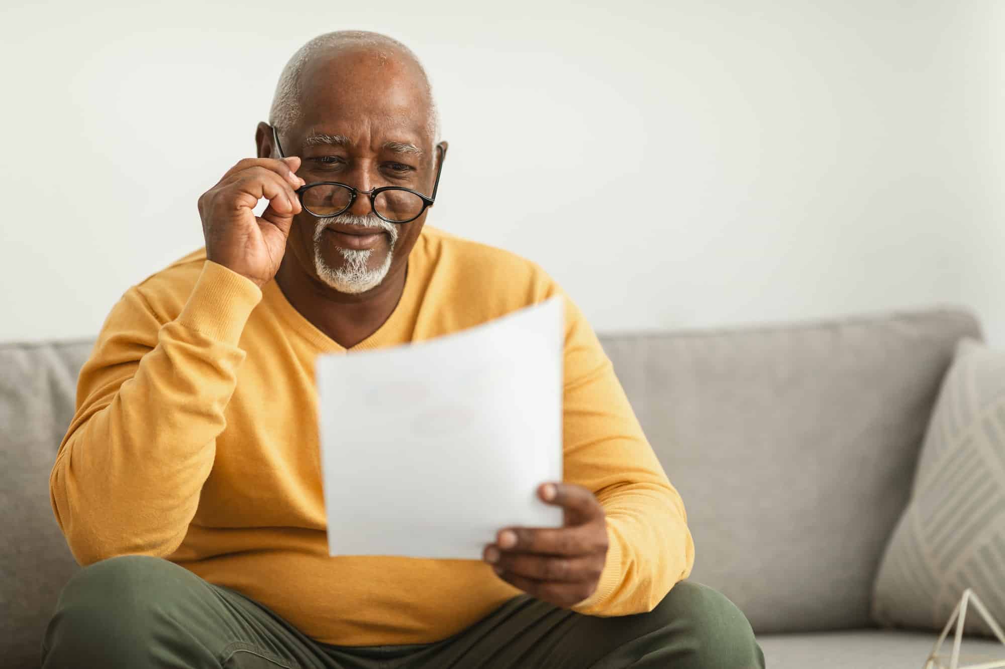 Contented Senior Black Man Reading Papers Wearing Eyeglasses At Home