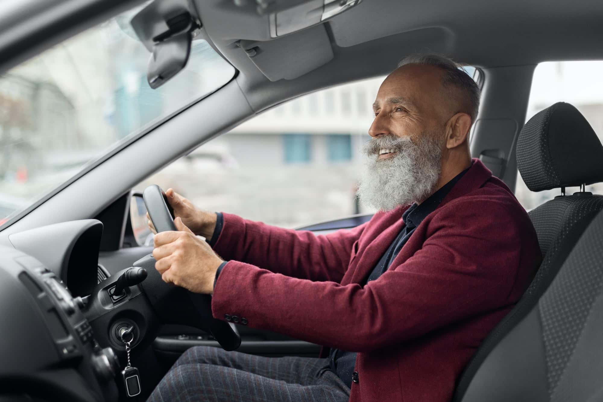 Joyful elderly grey-haired man driving new car, traveling alone