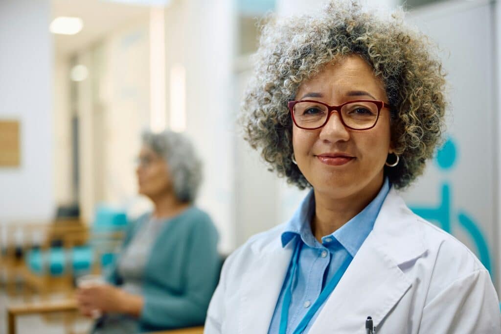 Portret van glimlachende vrouwelijke arts in medische kliniek die in de camera kijkt | Medisch keuring | Rijbewijsdokter