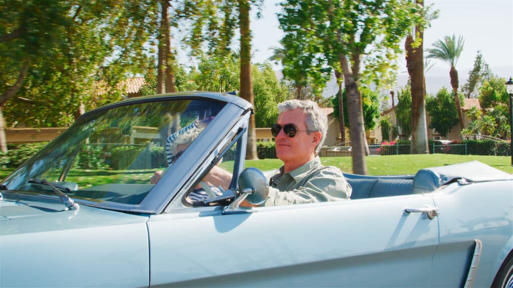 Zijaanzicht van een ouder echtpaar op roadtrip in een klassieke cabriolet | wachttijd verlengen rijbewijs 75 plus | Rijbewijsdokter